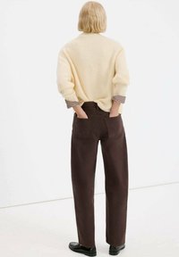 Jasnobeżowy sweter z dzianiny z podwiniętymi mankietami, zestawiony z wysokojakościowymi ciemnobrązowymi spodniami z kieszeniami z tyłu. Gładka faktura tkaniny.