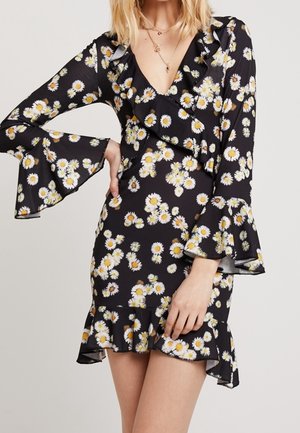 Robe portefeuille noire à fleurs, manches longues évasées et ourlet volanté, ornée de motifs de marguerites blanches et jaunes.