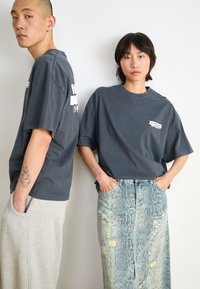 Gray oversized t-shirts with white lettering, paired with a snake-patterned denim skirt. Soft fabric and relaxed fit highlighted, along with pockets.