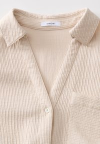 Chemise beige texturée à boutons avec col et poche poitrine, portant le label OPUS, avec un tissu doux et léger.