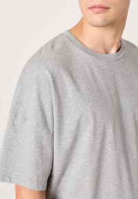 Šedé tričko s kulatým výstřihem vyrobené z měkké bavlněné směsi, s krátkými rukávy a volným střihem, s hladkou texturou a jednoduchým designem.