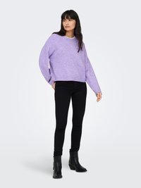 Ljuslila, oversize tröja med sänkta axlar, kombinerad med svarta skinny jeans och ankelstövlar. Slät stickad textur, avslappnad passform.