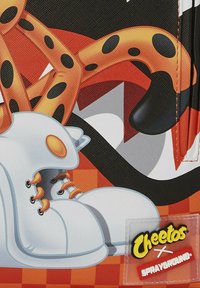 Zapatillas blancas con acentos naranjas y cordones negros, con un diseño de personaje de dibujos animados sobre un fondo texturizado y colorido. Logotipo de Cheetos visible.