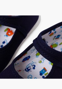 Navy Canvas-Schuhe haben eine runde Zehenpartie, einen elastischen Riemen und ein farbenfrohes Futter mit Mustern von Autos und Tieren auf einem weißen Hintergrund.