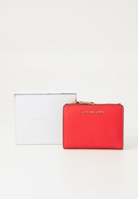 Portefeuille en cuir rouge avec une texture, matériel en or et logo embossé. Livré avec une boîte blanche de marque. Forme rectangulaire compacte.