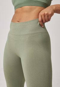 Leggings high-waisted di colore verde chiaro realizzati in un tessuto elastico. Presentano una cintura liscia e rigata e un design attillato con dettagli testurizzati.