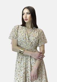 Abito stampato floreale in morbido tessuto beige. Caratterizzato da maniche corte a sbuffo, vita arricciata e delicati motivi floreali multicolori.