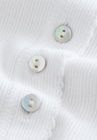 White textured fabric with vertical ribbing and three small pearlescent buttons sewn in a vertical line.