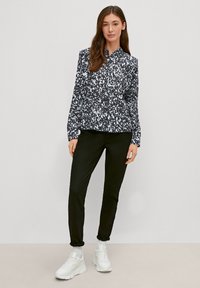 Langarm blouse met een zwart-wit abstract patroon, knoopkraag, gecombineerd met zwarte broeken en witte sneakers.