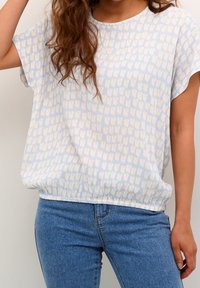 Haut bleu clair à manches courtes avec un motif texturé de formes crème douces, présentant un col arrondi et une coupe décontractée à la taille.