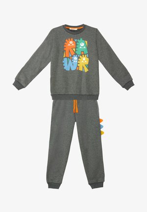 Grijze fleece trainingspak met een kleurrijke monsterafbeelding op de sweatshirt. De broek heeft een oranje trekkoord en kleurrijke accenten aan de zijkant.