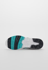 Sulan av en sneaker med svarta, teal och vita mönster och märkesnamnet Asics präglat i den vita midjedelen.