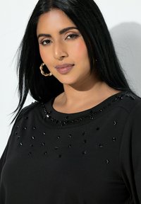 Czarna bluza z ozdobnymi czarnymi koralikami przy dekolcie. Miękki materiał, okrągły kołnierz i długie rękawy. Charakteryzuje się dopasowanym krojem.