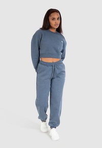 Niebieska krótka bluza i dopasowane spodnie dresowe o miękkiej teksturze i elastycznych mankietach, w zestawieniu z białymi sneakersami.