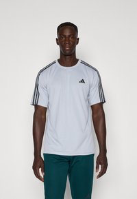 Lichtgrijs sport t-shirt met zwarte drie-streep accenten op de schouders en een klein zwart logo op de borst. Gemaakt van ademende stof.
