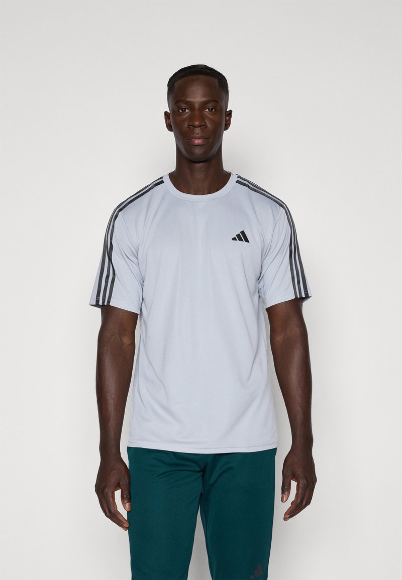 Lichtgrijs sport t-shirt met zwarte drie-streep accenten op de schouders en een klein zwart logo op de borst. Gemaakt van ademende stof.