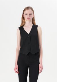 Musthave mustamata käisev särk struktuurse kangaga, millel on V-kaelus ja viis nööpaukku, lõikega, mis on kohandatud ja veidi lühem. Sobitatud mustade pükstega.