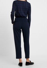 Granatowa koszula w kratę z długim rękawem, z niebieskimi i czerwonymi akcentami, zestawiona z dopasowanymi ciemnoniebieskimi spodniami z kieszeniami i gładką teksturą.