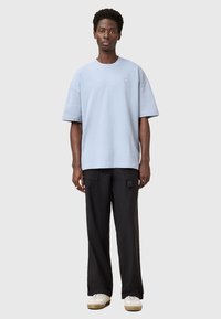 Lichtblauw oversized T-shirt van katoen, voorzien van een klein logo-detail, gecombineerd met zwarte wijde broek en witte sneakers.