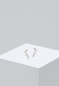 Orecchini a bottone in argento sterling con forme curve e allungate e accenti testurizzati, esposti su un piedistallo bianco.