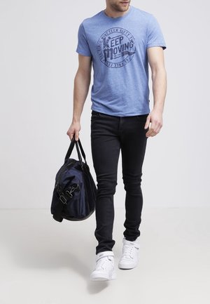 T-shirt bleu à manches courtes avec un graphique "Keep Moving", jean slim noir, baskets blanches, et un sac de sport noir.