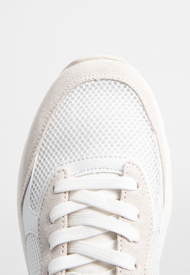 Weiße Sneaker aus Mesh- und Wildledermaterialien. Auffälliges Schnürsystem, runde Zehenpartie und strukturierte Akzente entlang der Seiten.