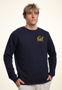 Felpa blu navy in misto cotone, con scollo rotondo e maniche lunghe. Sul davanti presenta il logo giallo "Cal" e il testo "University of California".