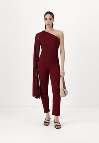 Mono burdeos de un solo hombro con un cuerpo ajustado y pantalones acampanados. Acompañado de un pequeño bolso crema y sandalias negras de tiras.