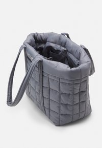 Sac en toile matelassé gris avec deux poignées, offrant un intérieur spacieux et une texture douce. Une couture notable crée un motif à carreaux.