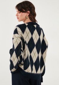 Maglione con un motivo a rombi navy, crema e verde. Realizzato in materiale morbido con una vestibilità rilassata e scollo a coste. Maniche accentuate.