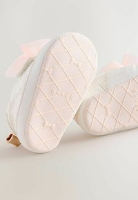 Scarpe bianche con una suola rosa strutturata, caratterizzate da un motivo trapuntato e un elegante fiocco rosa. Il tacco presenta un piccolo dettaglio con logo dorato.