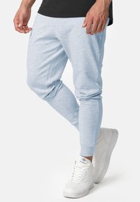 Lichtgrijze joggingbroek van zacht materiaal, met taps toelopende pijpen, elastische boorden en een gladde textuur, gecombineerd met witte sneakers.