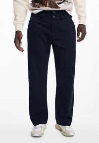 Pantaloni dritti blu navy con una trama liscia e chiusura con bottone. Abbinati a scarpe da ginnastica leggere.