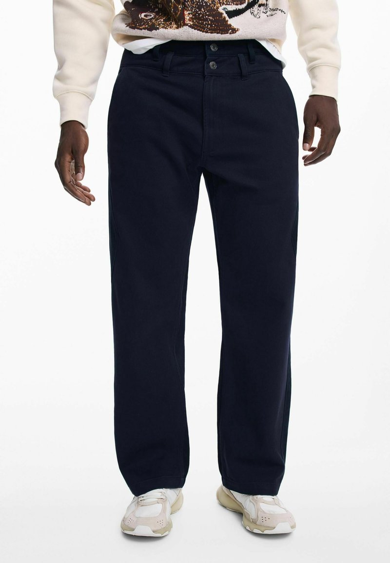 Pantaloni dritti blu navy con una trama liscia e chiusura con bottone. Abbinati a scarpe da ginnastica leggere.
