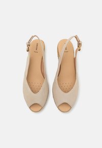 Zapatos tipo slingback en color beige con punta abierta, material de ante, plantilla perforada y acento de hebilla dorada. Suela plana con acabado texturizado.
