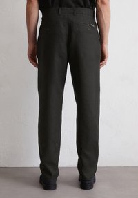 Mannen donker groene linnen broek met een rechte pasvorm, twee achterzakken en subtiele stikdetails, tegen een effen achtergrond.