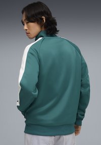 Αθλητικό μπουφάν σε τυρκουάζ με λευκές λεπτομέρειες στους ώμους. Διαθέτει ψηλό γιακά, ριμπ μανσέτες και υφή υφάσματος. Κοντά εφαρμοστό σχέδιο.