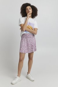 Lilla mønstrede nederdel med en smocket talje, parret med en hvid t-shirt med grafisk tryk, båret med hvide sneakers.