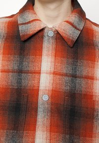 Rood geruite shirt met een knoopsluiting, zachte textuur, grote kraag en een voorzak met een zilveren knoopdetail.