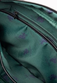 Grøn stofindvendig del af en taske med en glat tekstur og et subtilt lilla mønster, samt en sort lynlås langs den øverste kant.