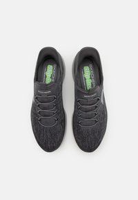 Zapatillas slip-on grises con parte superior de tela texturizada, cordones elásticos, cuello acolchado y logo verde en contraste en la plantilla.