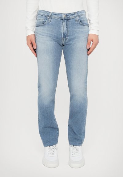 Jean en denim bleu clair à coupe droite, avec une taille mi-haute, un design à cinq poches et une texture légèrement délavée. Portés avec des baskets blanches.