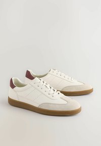 Hvide lædersneakers med en beige ruskinds tåhætte, burgundy hælaccent og perforerede side detaljer, sat på en brun gummisål.