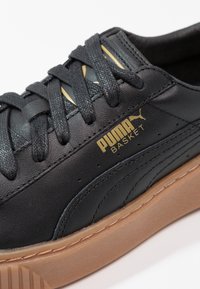 Baskets Puma Basket en cuir noir avec lacets noirs, logo doré et semelle en gomme visibles de côté et de dessus.