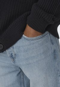 Navy ribbed knit cardigan with a button detail, worn over light blue denim jeans featuring a slight distressing at the pocket.