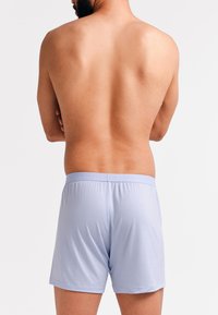 Lichtblauwe boxershorts met elastische tailleband, met een gladde textuur en casual pasvorm, gezien vanaf de achterkant met een neutrale achtergrond.