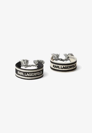 Two woven bracelets in black and cream, featuring "KARL LAGERFELD" text. Each has decorative tassels at the ends and a smooth texture.