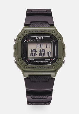 Montre numérique avec un boîtier en résine verte, un bracelet en caoutchouc noir et un afficheur LCD indiquant l'heure et la date. Les caractéristiques incluent une alarme et une résistance à l'eau.