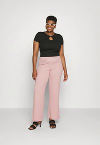 Top preto justo com corte em forma de lágrima, combinado com calças largas rosa claro. Acessórios incluem óculos de sol brancos e sandálias de salto pretas.