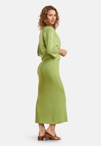 Groene geribbelde gebreide tweedelige outfit met een cropped top met 3/4 mouwen en een lange, aansluitende rok. Draag het met bruine sleehakken.